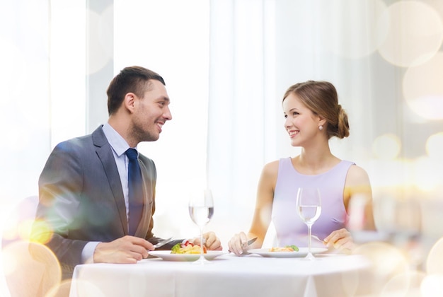 restaurante, pareja y concepto de vacaciones - pareja sonriente comiendo plato principal en el restaurante