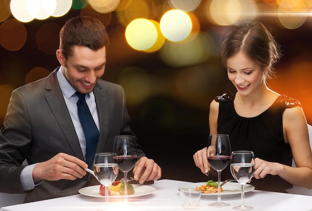 restaurante, pareja y concepto de vacaciones - pareja sonriente comiendo plato principal con vino tinto en el restaurante