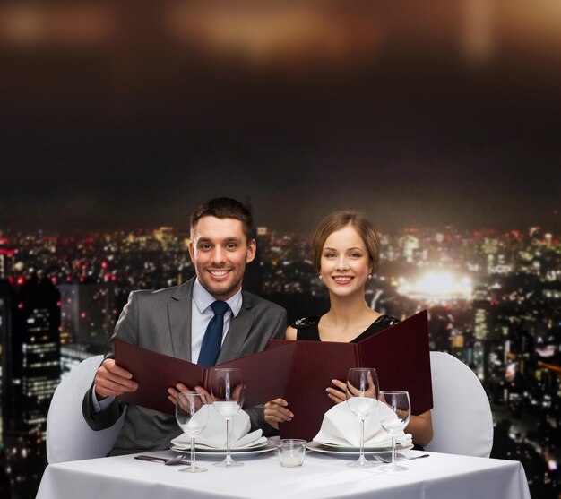 restaurante, pareja y concepto de vacaciones - pareja sonriente con menús en el restaurante