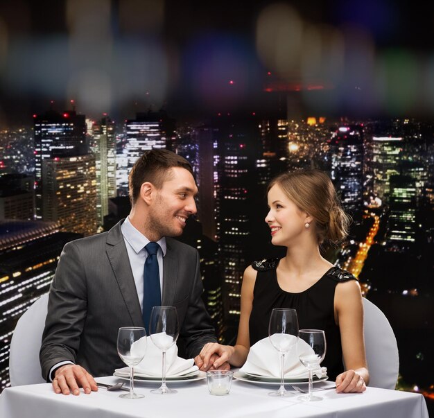 restaurante, pareja y concepto de vacaciones - pareja sonriente mirándose en el restaurante