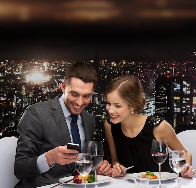 restaurante, tecnologia, casal e conceito de férias - casal sorridente tirando foto do prato principal com câmera do smartphone no restaurante