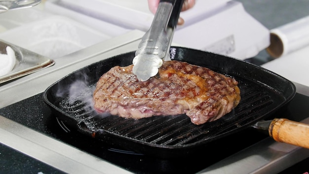 Restaurantküche, die ein Steak in der Pfanne brät, ein Koch, der das Fleisch umdrehen will