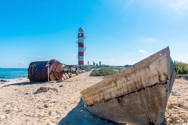 Restos de boya náutica y barco en la playa con turistas alrededor del faro