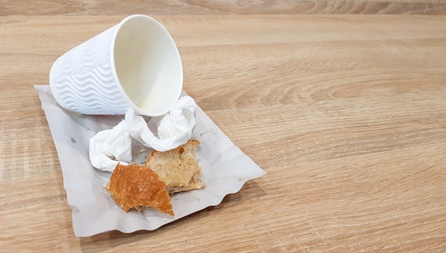 Restos de comida em um prato de papel e a xícara de café de papel sujo vazio em uma mesa de madeira em um café de fast food.