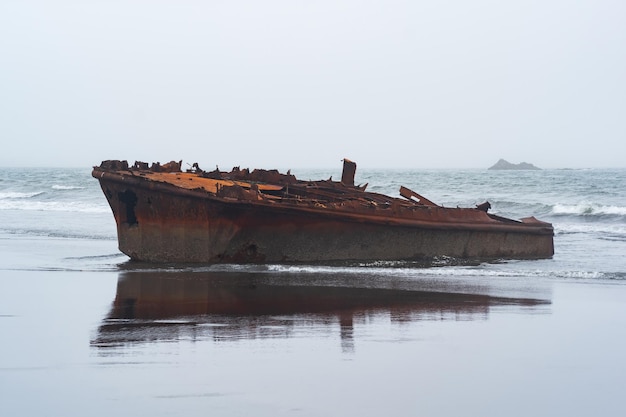 Restos de naufrágio enferrujados de um navio lavado em terra contra uma paisagem nevoenta