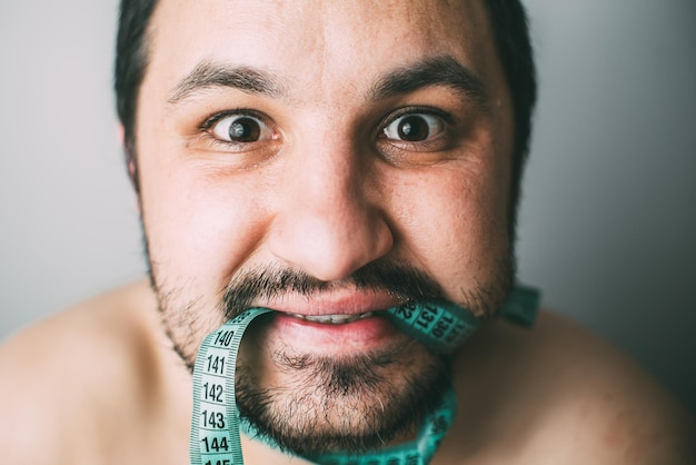 Foto restrição de dieta e conceito de estresse retrato de jovem frustrado com uma fita métrica verde em volta da boca isolada no fundo da parede cinza emoção de expressão facial