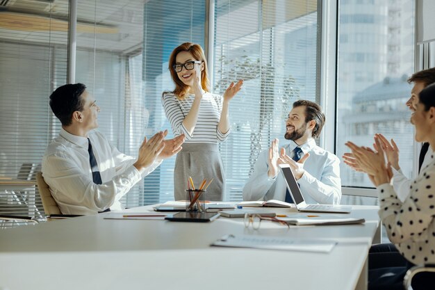 Resultado perfecto. Compañeros jóvenes optimistas aplaudiendo mientras celebran el exitoso final de su proyecto en la reunión mensual