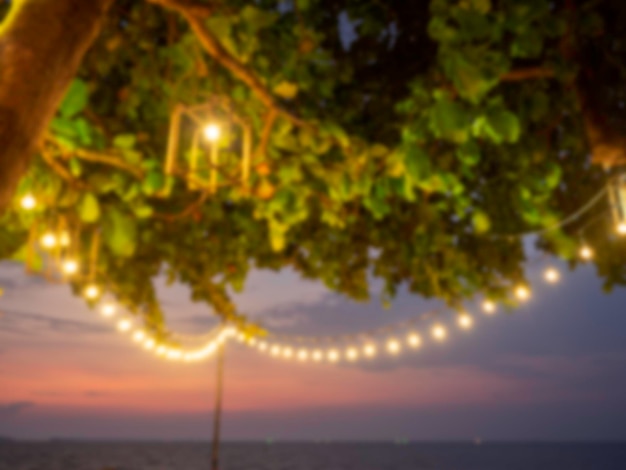 Resumen borroso de lámpara y bombilla colgante bokeh en el fondo del árbol en luces de cadena amarillas al atardecer con decoración bokeh en restaurante al aire libre en la fiesta nocturna