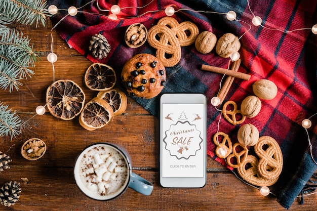 Resumen de la página de inicio de la venta navideña de la tienda en línea en un teléfono inteligente rodeado de bebidas calientes, dulces y nueces