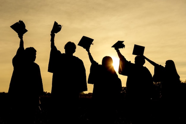 Foto resumen primer plano grupo de vista trasera de los graduados universitarios en la puesta de sol de silueta