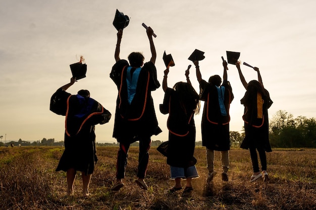 Foto resumen primer plano grupo de vista trasera de los graduados universitarios en la puesta de sol de silueta