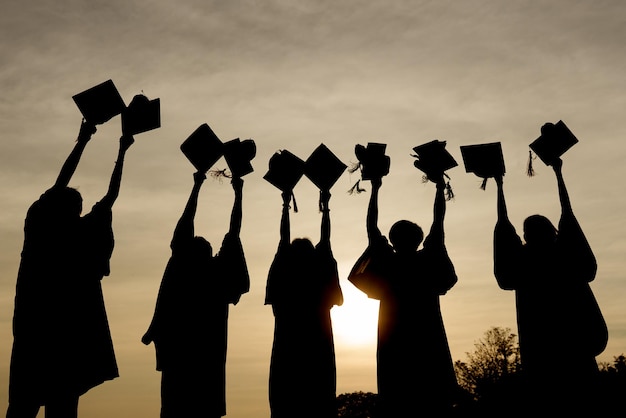 Foto resumen primer plano grupo de vista trasera de los graduados universitarios en la puesta de sol de silueta