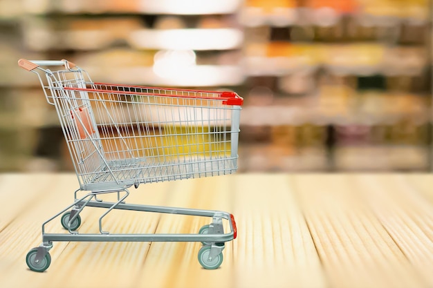 Resumo desfocado prateleiras de supermercado fundo desfocado com carrinho de compras na mesa de madeira