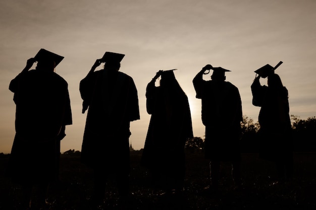 Foto resumo fechar o grupo de visão traseira dos graduados universitários no pôr do sol silhouette