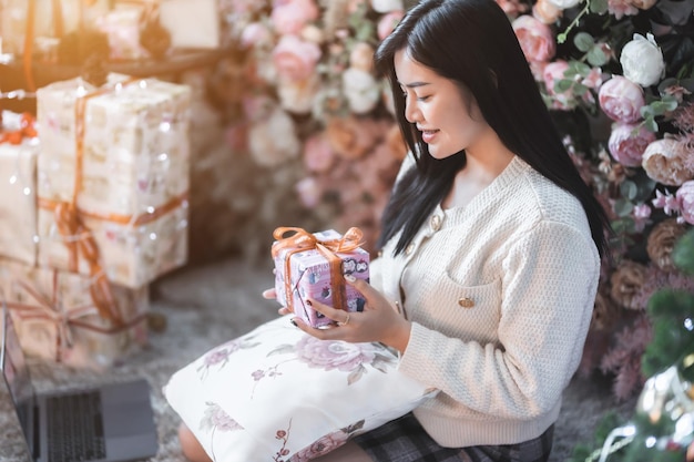 Retrata a una hermosa joven asiática que usa ropa abrigada intercambiando regalos y da un regalo en casa en la sala de estar o en el café Durante las vacaciones de Navidad y Año Nuevo