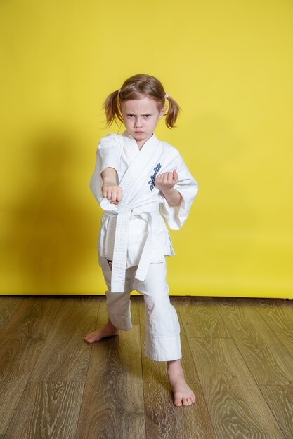 Retrato de 5 años niña caucásica en kimono practicando Karate contra el fondo amarillo en casa