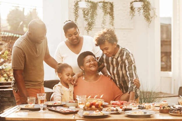 Retrato de abuela afroamericana feliz celebrando cumpleaños con familia durante la cena al aire libre ...