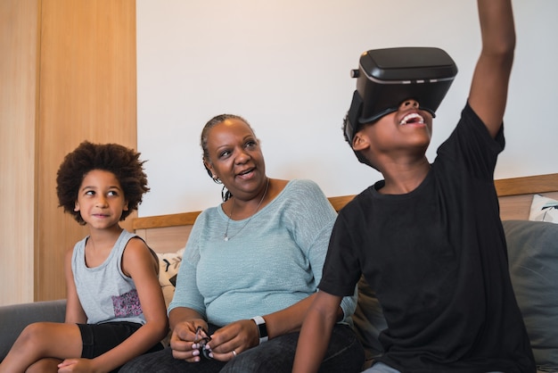 Retrato de abuela afroamericana y nietos jugando junto con gafas VR en casa. Concepto de familia y tecnología.