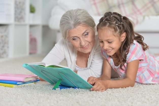 Retrato de abuela con una linda niña haciendo los deberes juntos mientras están acostados en el suelo