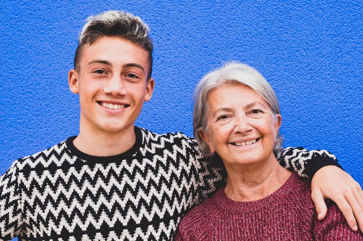 Retrato de una abuela de pelo blanco y un nieto adolescente sonriendo y abrazando mirando a la cámara