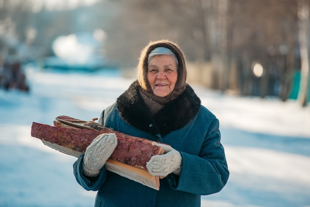 Retrato de la abuela rusa, en el pueblo en invierno, preparando leña, en Siberia.