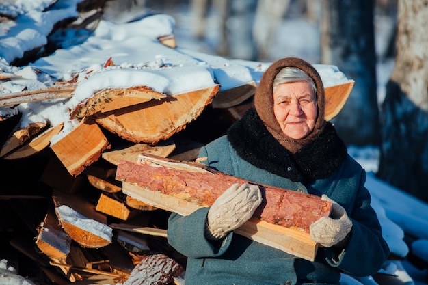 Retrato de la abuela rusa, en el pueblo en invierno, preparando leña, en Siberia.