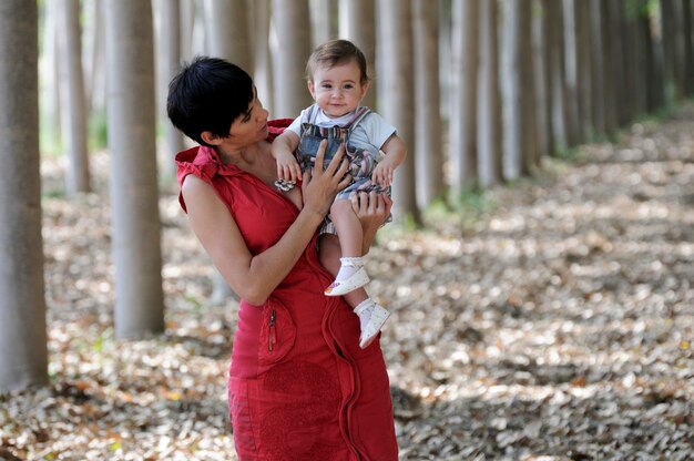 Foto retrato de la abuela sosteniendo a su nieta mientras está de pie en medio de los árboles en el bosque