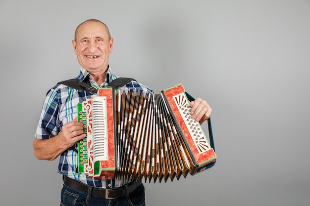 Retrato de un abuelo hombre toca el acordeón sobre un fondo gris