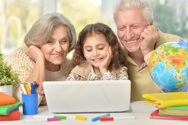 Retrato de abuelos felices y una niña usando laptop