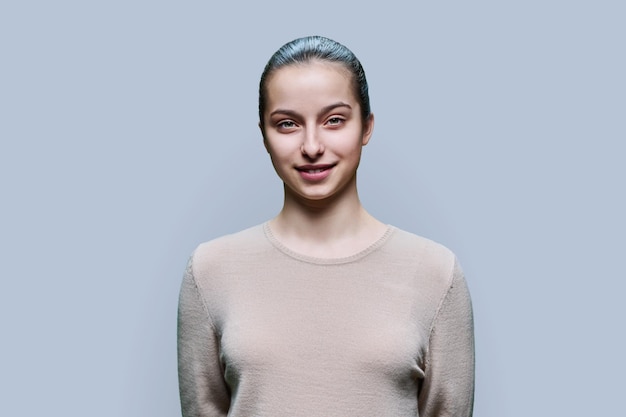 Foto retrato de una adolescente de 15 y 16 años sonriendo mirando a la cámara sobre un fondo gris