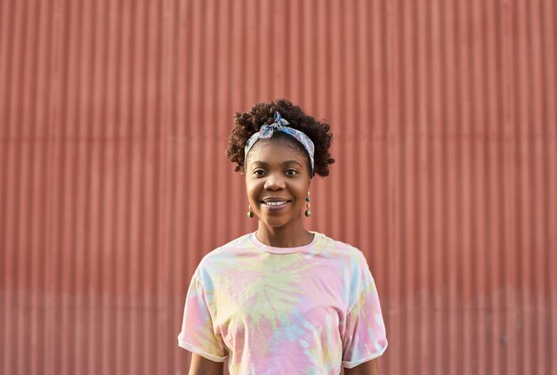 Retrato de adolescente africano sonriente de pie contra la pared roja al aire libre