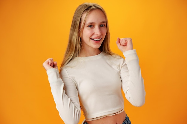 Retrato de una adolescente alegre y feliz celebrando el éxito con fondo amarillo