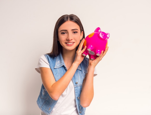 Retrato del adolescente alegre de la muchacha que sostiene un cerdo rosado.