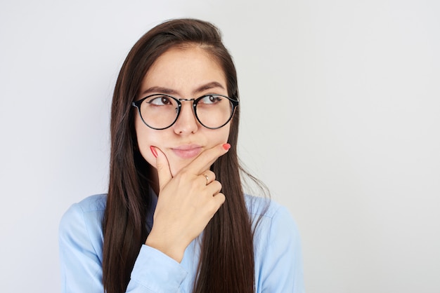 Retrato de adolescente asiático en gafas con cara pensativa toma una decisión, pensando, se ve perplejo en blanco con espacio de copia