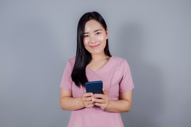 Retrato de adolescente asiático sonriente está utilizando teléfono móvil o smartphone sobre fondo gris