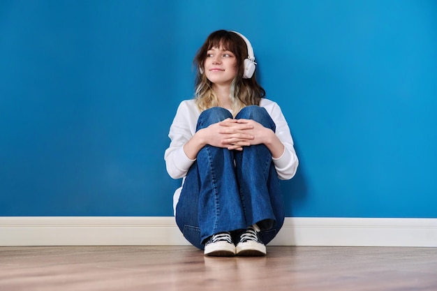 retrato, de, adolescente, en, auriculares, sentado, en, piso, en, fondo azul