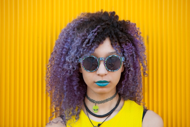 Retrato de un adolescente con cabello afro y labios azules en una pared amarilla