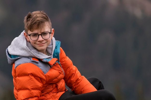 Retrato de un adolescente con cabello castaño con gafas y chaqueta deportiva de otoño. Guy mira a la cámara y sonríe.