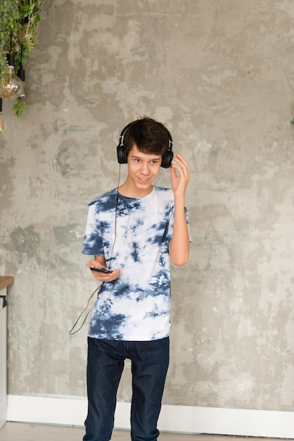 Retrato de un adolescente con una camiseta y jeans escuchando música con auriculares