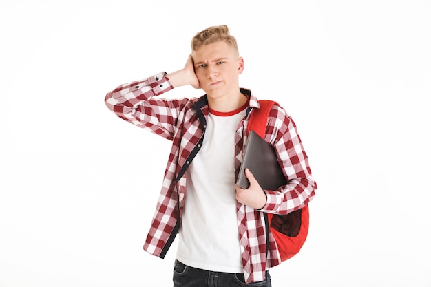 Retrato de un adolescente caucásico con camisa a cuadros expresando confusión o problema en la cara y sosteniendo portátil plateado, aislado sobre la pared blanca