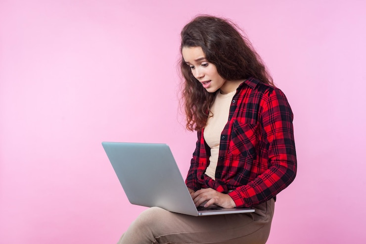 Foto retrato de una adolescente disgustada con cabello castaño rizado en camisa a cuadros preocupada por los problemas de la computadora portátil falla del software que parece desesperada e indefensa foto de estudio aislada en un fondo rosa