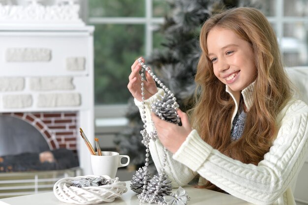 Retrato de una adolescente feliz con adornos navideños sentados a la mesa en casa