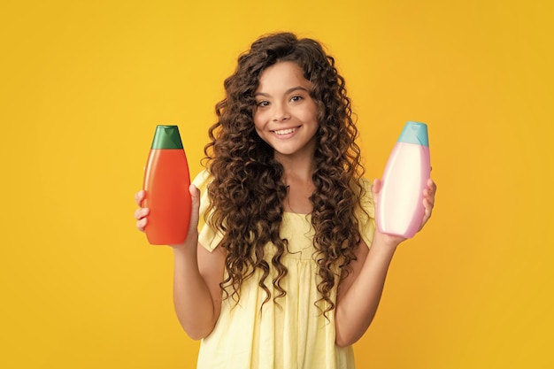 Retrato de adolescente feliz de una niña con una botella de acondicionador de champú o gel de ducha para el cuidado del cabello de los niños