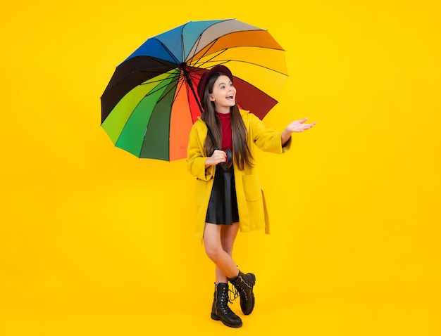 Retrato de adolescente feliz Retrato de adolescente feliz Niña adolescente bajo el paraguas del arco iris en el clima de otoño aislado sobre fondo amarillo Ropa de niños de otoño Niña sonriente en abrigo de otoño