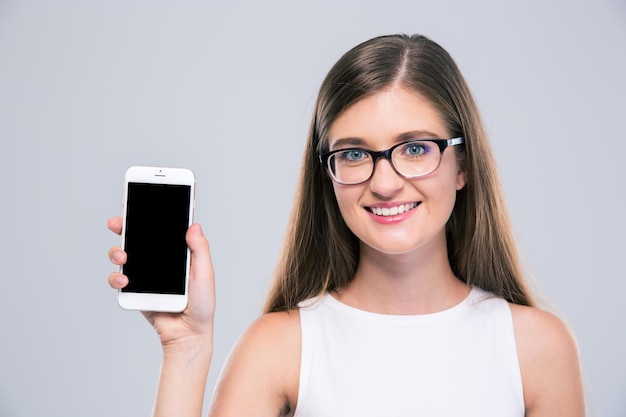 Foto retrato de una adolescente femenina sonriente con gafas mostrando la pantalla del teléfono inteligente en blanco aislado