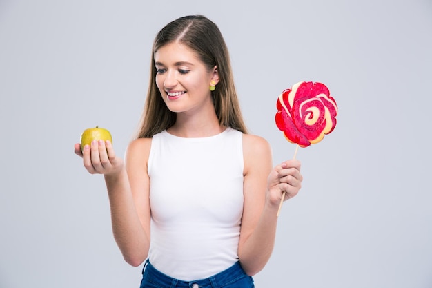 Retrato de una adolescente femenina sonriente sosteniendo manzana y piruleta aislado