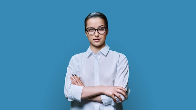 Foto retrato de una adolescente con gafas y brazos cruzados sobre un fondo azul