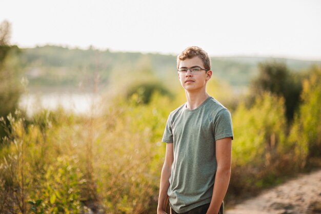 Retrato de un adolescente con gafas y una camiseta verde en el contexto de la naturaleza en el