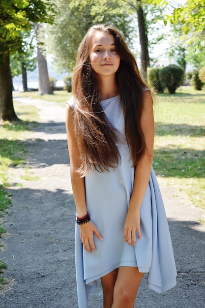 El retrato de la adolescente hermosa en blusa azul, contra el verde del parque del verano juega con su pelo.