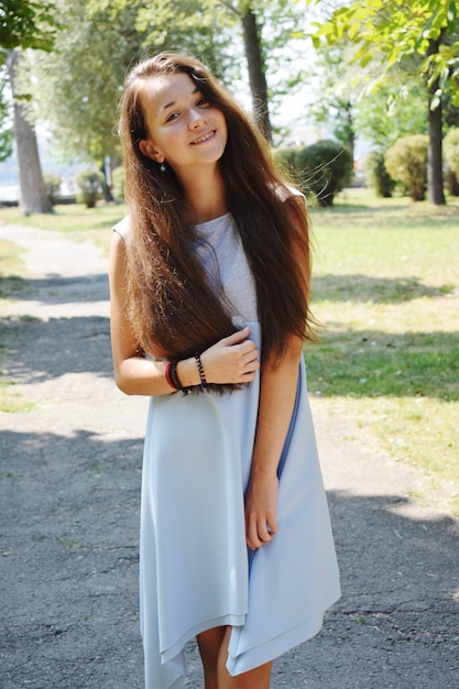 El retrato de la adolescente hermosa en blusa azul, contra el verde del parque del verano juega con su pelo.